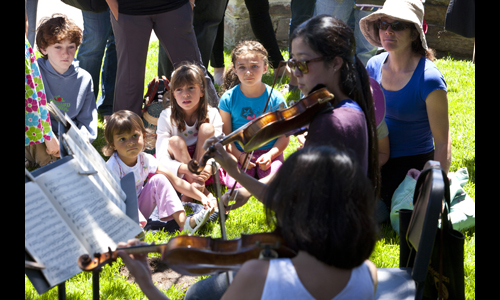 Youngsters enjoy a string demonstration outdoors during the Tour of the Orchestra. Photo: rr jones