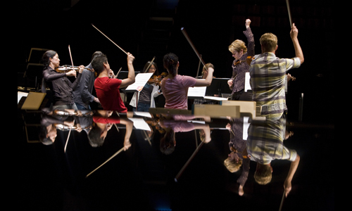 Marin and her eight-violin ensemble, reflected in the “pool” of a lacquered piano lid. Photo: rr jones